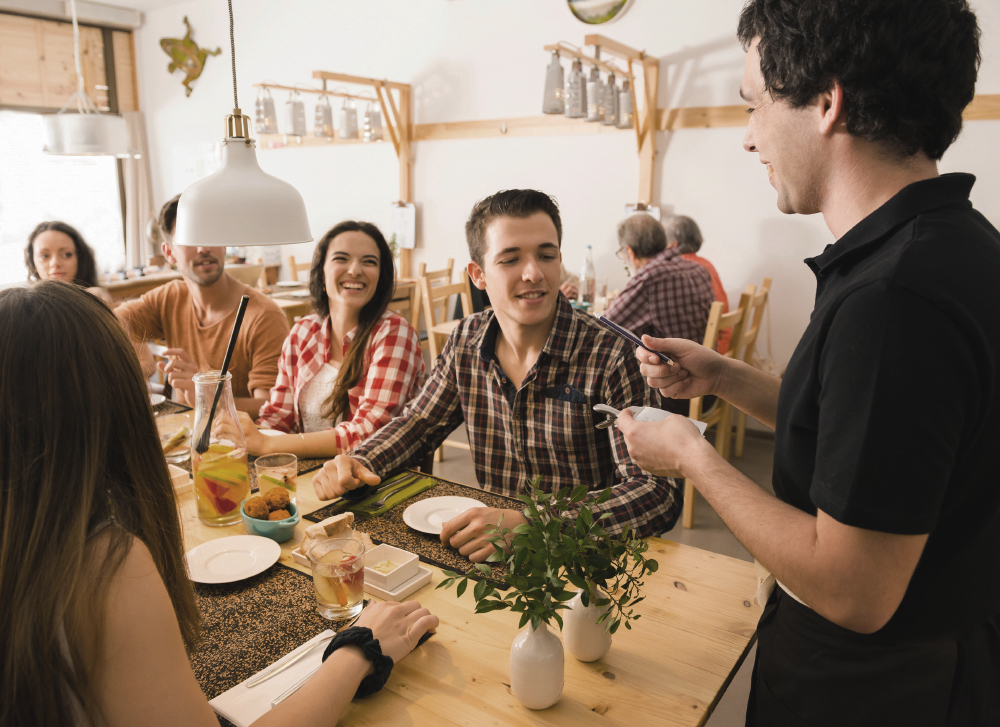 Group of friends at the restaurant and being served by the waiter